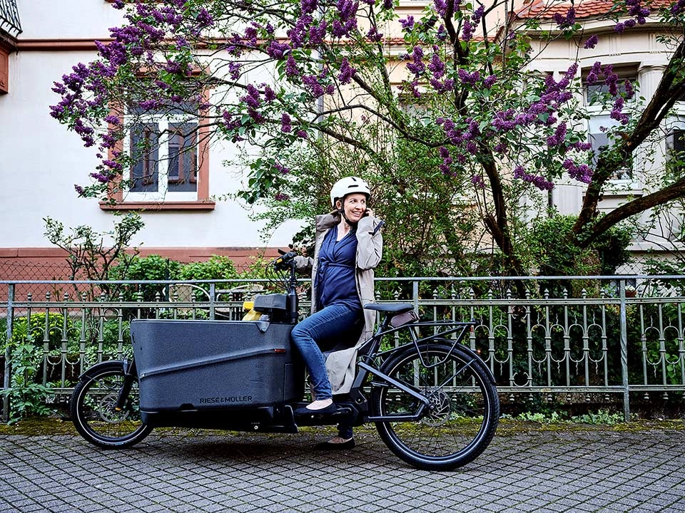 Eine JobRadlerin auf dem Lastenrad blickt zurück auf ihr Handy